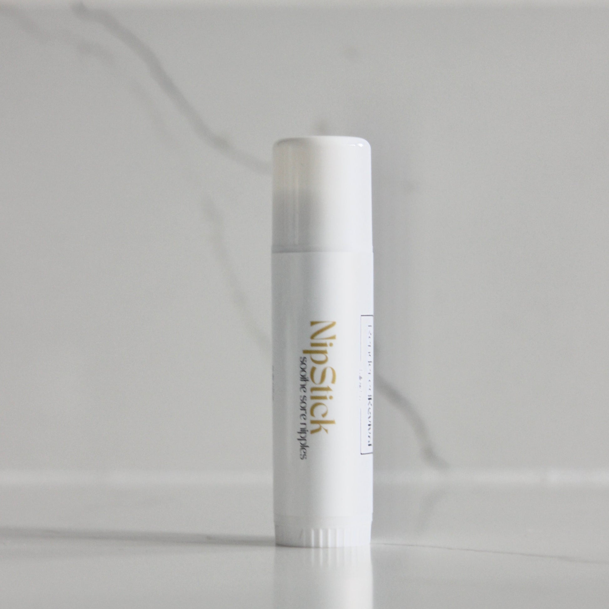 0.5 oz nip stick, a skincare essential, presented in a sleek white tube adorned with a white label and vibrant yellow font, standing upright with elegance and simplicity against a clean background