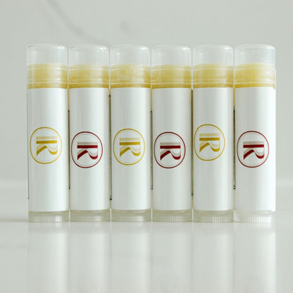 Elevate your lip care routine with our exquisite collection of clear lip balm tubes. Proudly displayed against a pristine white quartz countertop, these six standing tubes showcase a harmonious blend of clarity and sophistication. Each tube features a distinctive white label adorned with our logo, alternating between vibrant red and sunny yellow accents. The minimalist design exudes a sense of purity and quality. Explore our natural skincare line where simplicity meets elegance. Lip care, redefined.